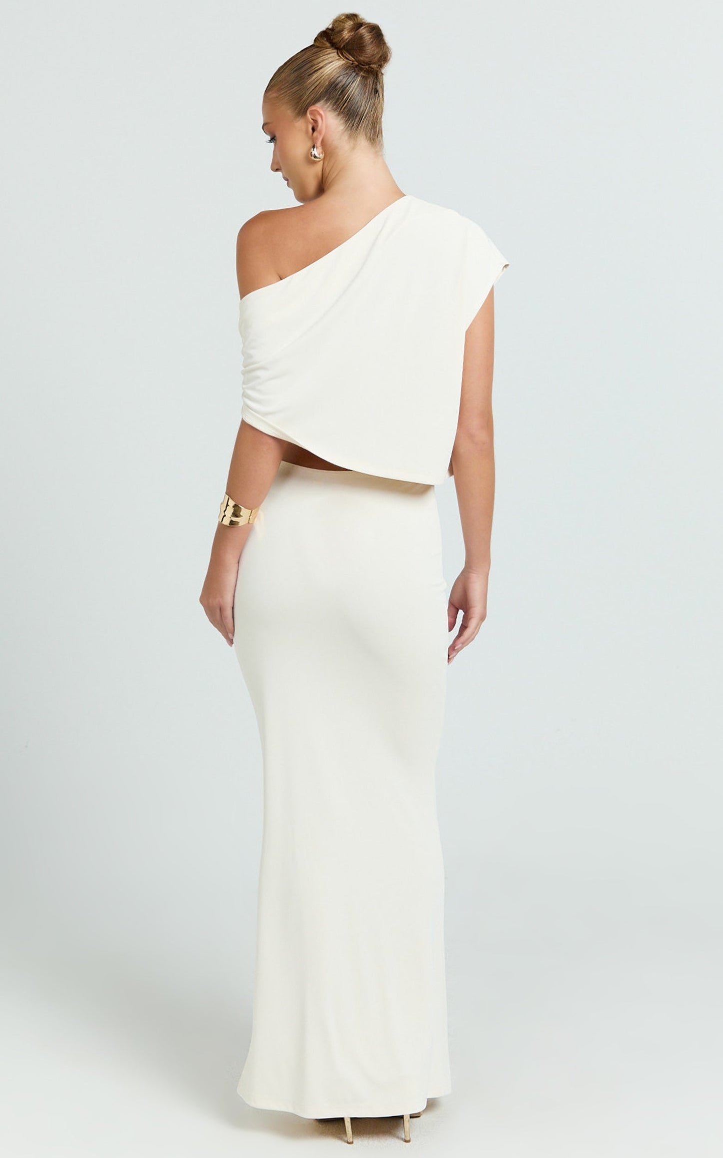 Conjunto de dos piezas: top asimétrico tipo capa y falda larga con adornos florales fruncidos en color marfil.